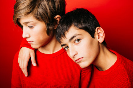 Two Pre-adolescent boys, wearing a red sweater, embracing over a red backgroundの写真素材