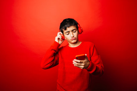 Pre-adolescent boy wearing a red sweater and red headphones over a red background, listening to music and dancingの写真素材