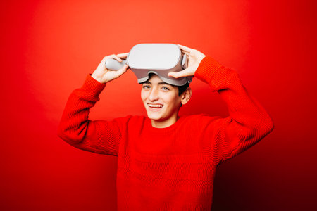 Pre-adolescent boy wearing in red over a red background playing video games with virtual reality glassesの写真素材