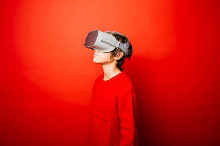 Pre-adolescent boy wearing in red over a red background playing video games with virtual reality glassesの写真素材
