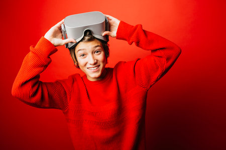 Pre-adolescent boy wearing in red over a red background playing video games with virtual reality glassesの写真素材