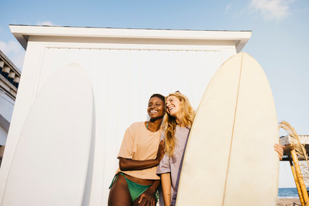 Portrait of two cheerful young women standing with their surfboards after a day off at the beach. Two female surfers in swimwear holding their surfboards.の写真素材