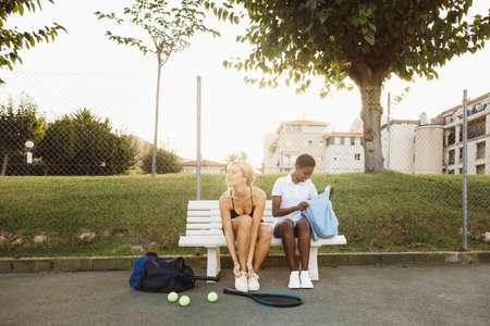 Young women getting ready on bench before a tennis game. Young women in tennis clothes getting ready on a tennis court.の写真素材