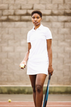 Portrait of a young beautiful women with tennis clothes and racket in a tennis court ready to play a game.の写真素材
