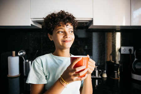 Ten years old girl with a red mug with milk in the kitchen looking away. Girl at home drinking a cup of milk.の写真素材
