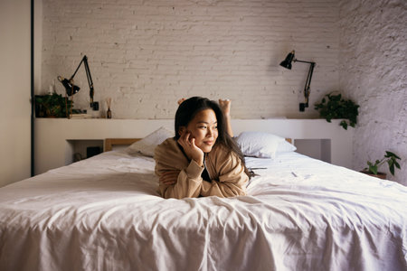 Portrait of young thoughtful woman lying on bedの写真素材