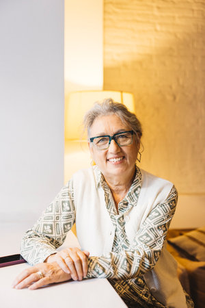 Portrait of senior smiling woman with glasses in living room at her home.の写真素材