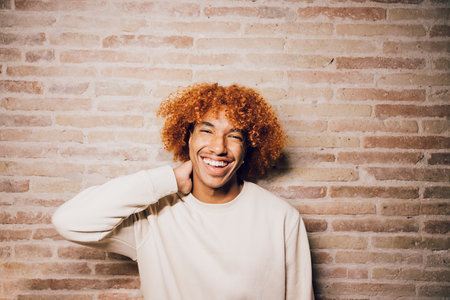Portrait of a smiling young african american man with afro hairstyle with a brick wall background.の写真素材