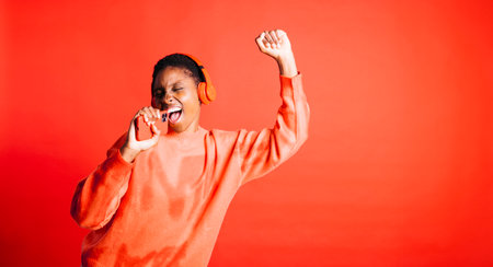 Happy young woman dancing with her arms raised while wearing wireless headphones in a studio. Woman listening to her favorite music playlists.の写真素材