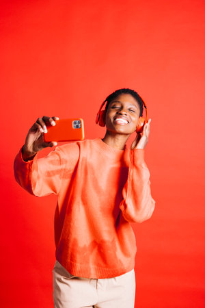 Happy young woman dancing and singing while wearing wireless headphones in a studio. Woman listening to her favorite music playlists.の写真素材