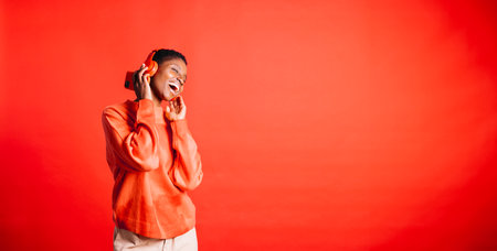 Happy young woman dancing and singing while wearing wireless headphones in a studio. Woman listening to her favorite music playlists.の写真素材