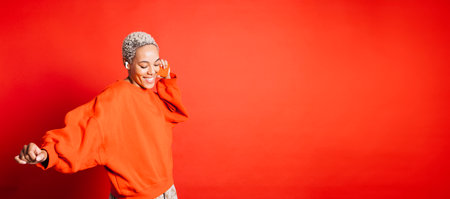 Happy young woman dancing while wearing wireless headphones in a studio. Woman listening to her favorite music playlists.の写真素材