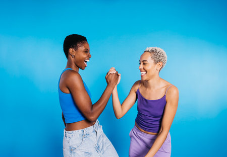 Two young cheerful women dancing in a studio with a blue background.の写真素材