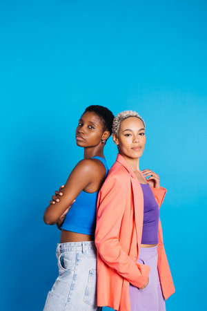 Portrait of a young female couple in front of a blue background at studio.Two women together at studio.の写真素材