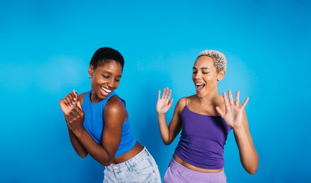 Two young cheerful women dancing in a studio with a blue background.の写真素材