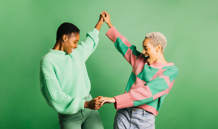 Two young cheerful women wearing green clothes and dancing in a studio with a green background.の写真素材