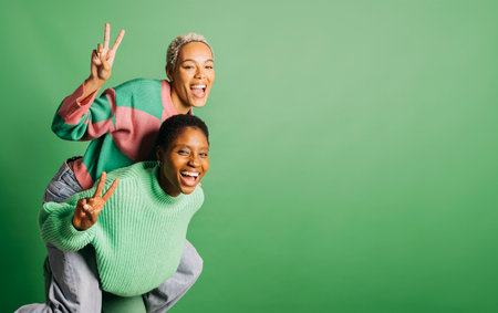 Two young playful women wearing green clothes embracing in a studio with a green background.の写真素材