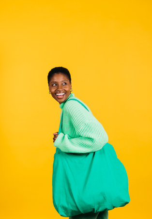 Portrait of a cheerful young beautiful woman wearing green clothes and a green bag standing against a yellow background. Young woman in studio looking at the camera.の写真素材