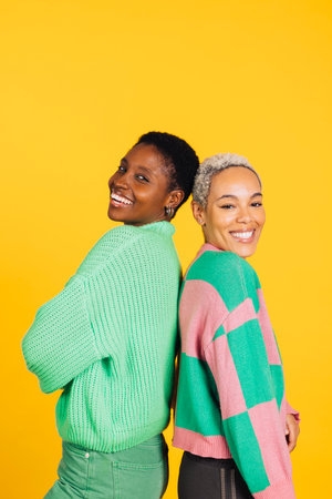 Two young cheerful women wearing green clothes embracing in a studio with a yellow background.の写真素材