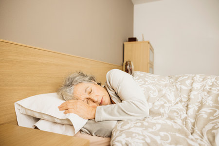 Sleeping senior woman in her bed in the early morning.の写真素材