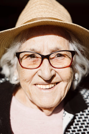 Portrait of a smiling ninety three years old woman with a straw hat under the sunlight.