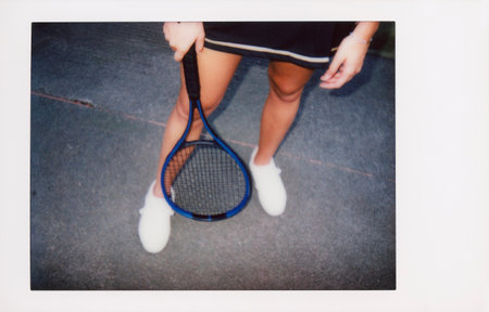 Low section of female tennis player holding racket while standing on tennis court