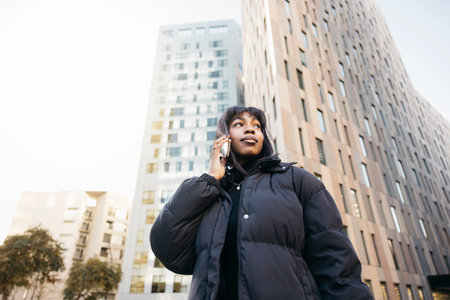 Young beautiful black woman wearing black clothes talking on a phone while walking on a city.の写真素材