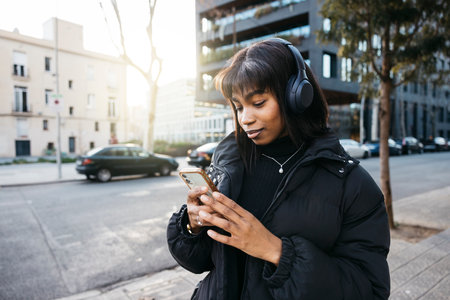 Young woman walking with wireless headphones and using a phone while walking on a city.の写真素材
