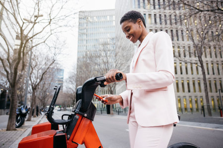 Stylish businesswoman using her mobile phone to rent a city bike on her way to work.の写真素材