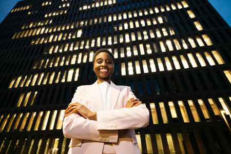 Young smiling black stylish businesswoman in front of a building looking at camera. Businesswoman on downtown district at night.の写真素材