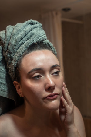 Girl looking in the mirror after a shower touching her faceの写真素材