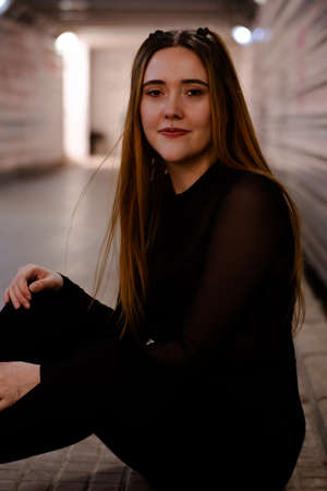 Long hair ginger girl sitting on the ground of subway tunnel looking at the cameraの写真素材