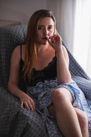 Woman sitting posing next to a window touching her lipsの写真素材
