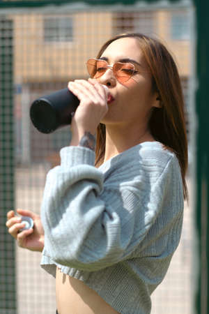 Girl with glasses of pink hearts drinking water from a bottle of black colorの写真素材