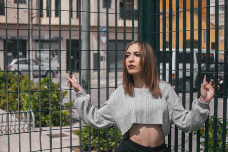 woman posing facing the sun on a green fence in a playgroundの写真素材