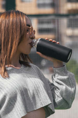 Closeup of a sporty girl drinking water from a black bottle wearing pink heart-shaped sunglasses.
