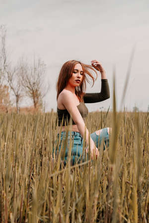 Young woman touching her hair in the middle of a field with her eyes closed and wearing fashionable clothesの写真素材