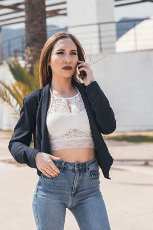 Business woman keeping an important call on mobile phone while having her hand in her jean pocketの写真素材