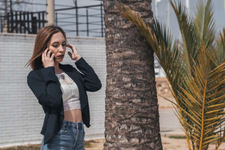 woman adjusts her hair while having a business phone call next to a palm treeの写真素材