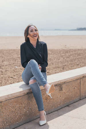 Elegant woman laughing sitting on a bench with the beach in the backgroundの写真素材