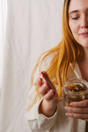 red-haired girl opening a jar of dried fruit on a light background with copy space