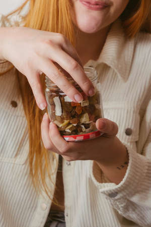 red-haired girl taking dehydrated fruit from a glass jarの写真素材