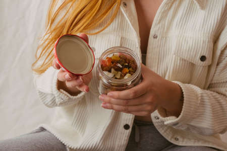 Horizontal closeup of hands of a red-haired girl opening a jar of dried fruit