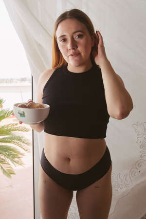 girl in summer pajamas holding a bowl with muffins in front of a window with natural lightの写真素材