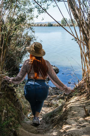 Traveler girl with straw hat walking on a path next to the riverの写真素材