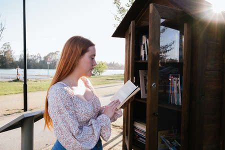 red-haired girl reading a book in an outdoor bookstore with a river in the backgroundの写真素材