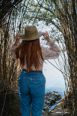 traveler woman with her hands on her straw hat looking at a river hidden between vegetationの写真素材