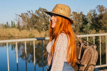 Traveler girl with backpack and straw hat smiling in natural environmentの写真素材