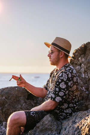 young man in profile with a casual hat smoking a joint in front of the seaの写真素材