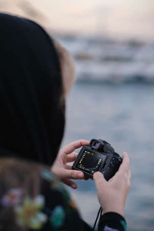 woman with her head covered by a scarf taking photos of a river with a cameraの写真素材